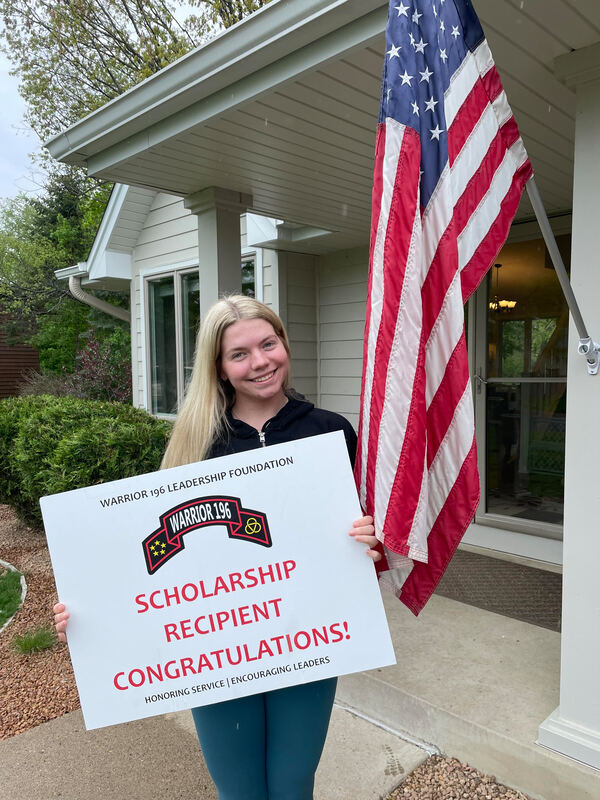 Scholarship recipient with Warrior 196 sign and USA flag